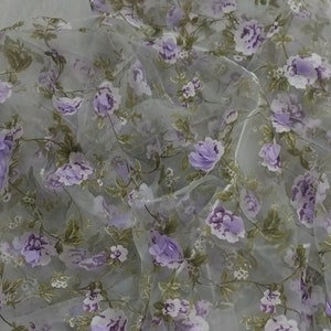 Könnte beinhalten: Ein durchsichtiger, hellgrauer Stoff mit einem zarten Blumenmuster in Violetttönen. Der Stoff ist durchscheinend und hat eine weiche, fließende Textur.