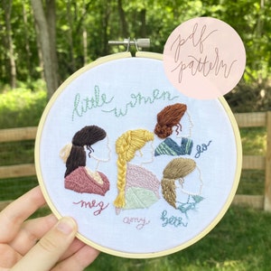 Op de afbeelding: Borduurwerk in een hoepel met de vier March-zussen uit Little Women. De hoepel is wit met een houten frame en heeft de namen Meg, Amy, Beth en Jo geborduurd in cursief. De zussen zijn in profiel afgebeeld met verschillende kapsels.