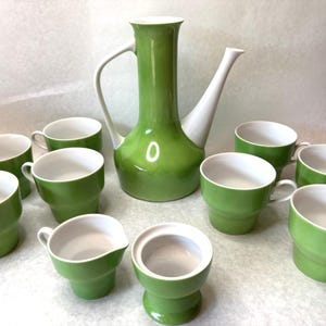 Op de afbeelding: Een vintage groene en witte keramische theeset. De set bevat een hoge, slanke theepot, verschillende theekopjes, een melkkan en een suikerpot. De kopjes en de theepot zijn felgroen, terwijl de tuit en het handvat van de theepot wit zijn.