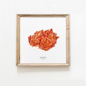 Könnte beinhalten: Ein gerahmter Druck eines roten und orangefarbenen Minerals namens Krokoit. Der Druck ist auf weißem Papier mit dem Namen des Minerals und seiner chemischen Formel "Krokoit, Chromat" unterhalb des Bildes.
