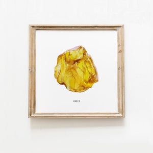 Puede incluir: Una pintura de acuarela de una piedra de ámbar amarilla. La piedra tiene una forma irregular y una apariencia translúcida. La pintura está enmarcada en un marco de madera clara y tiene la palabra "ÁMBAR" impresa debajo de la piedra.