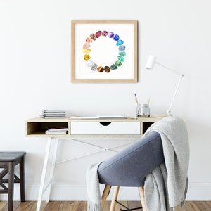 May include: A framed print of a colorful circle of gemstones, with each stone representing a different color of the rainbow. The print is hanging on a white wall above a desk with a chair and a lamp.