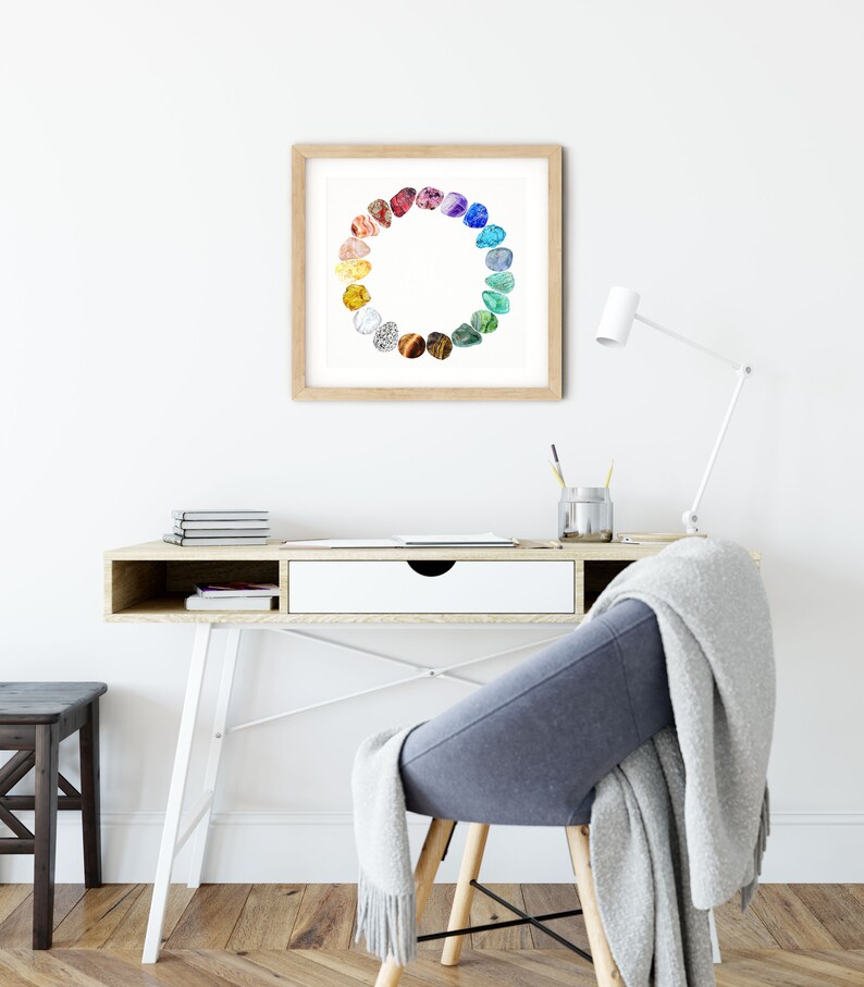 May include: A framed print of a colorful circle of gemstones, with each stone representing a different color of the rainbow. The print is hanging on a white wall above a desk with a chair and a lamp.
