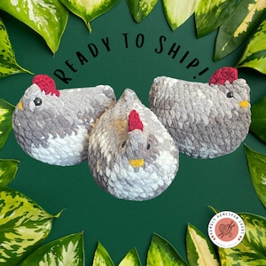 May include: Three handmade crochet chickens in shades of gray, white, and yellow, with red combs. The chickens are arranged on a dark green background, surrounded by green and yellow leaves. The text "READY TO SHIP!" is above the chickens.