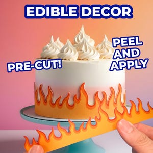 May include: A round cake topped with white frosting swirls, decorated with an orange and yellow flame-patterned edible border. The text EDIBLE DECOR, PRE-CUT!, and PEEL AND APPLY are visible. A hand holds an additional flame-patterned strip.