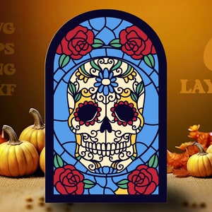Puede incluir: Un diseño de vitral colorido de una calavera de azúcar con acentos florales. La calavera está rodeada de un fondo azul y rosas rojas. El diseño es de estilo vitral con contornos negros.