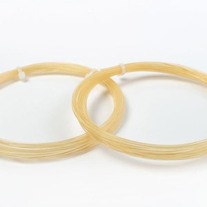 May include: Two spools of natural-colored tennis string, each wrapped in a circle.