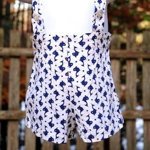 May include: White overalls with blue fish print. The straps have a button closure.