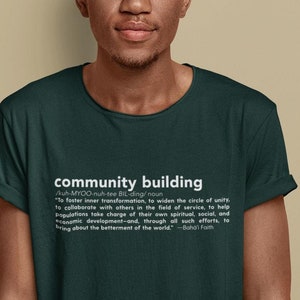 May include: A man wearing a dark green t-shirt with the definition of "community building" printed on the front. The text is in white and includes the word "community building" in a larger font size.