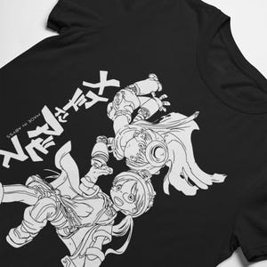 以下が含まれることがあります： 黒いTシャツに、2人のアニメキャラクターが躍動感あふれるポーズで描かれた白いグラフィック。日本語の文字と「MADE IN ABYSS」の文字がプリントされています。デザインは詳細な線画です。