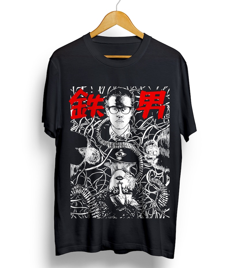 Pode incluir: Camiseta preta com uma estampa gr&aacute;fica branca e preta de um homem de &oacute;culos e uma mulher com um olho na testa. O texto "鉄男" est&aacute; impresso em vermelho na camiseta.