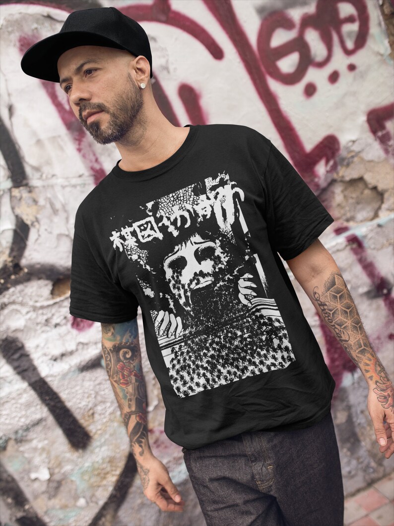Puede incluir: Una camiseta negra con un estampado gr&aacute;fico blanco de una cara rodeada de una multitud de personas. El gr&aacute;fico tambi&eacute;n incluye texto japon&eacute;s.