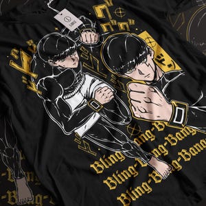 May include: Black t-shirt featuring a dynamic anime-style illustration of a character in a fighting pose. The design includes gold accents and the text "Bling-Bang-Born". A tag with the text "LABCE" is visible.