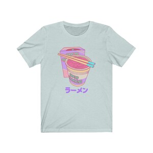 May include: A light blue t-shirt with a cartoon illustration of a pink and purple instant noodle cup with chopsticks and a box that says "Seasoned Noodles" and "Soup Noodles" in a pink and green font. The text "ラーメン" is printed in purple below the illustration.