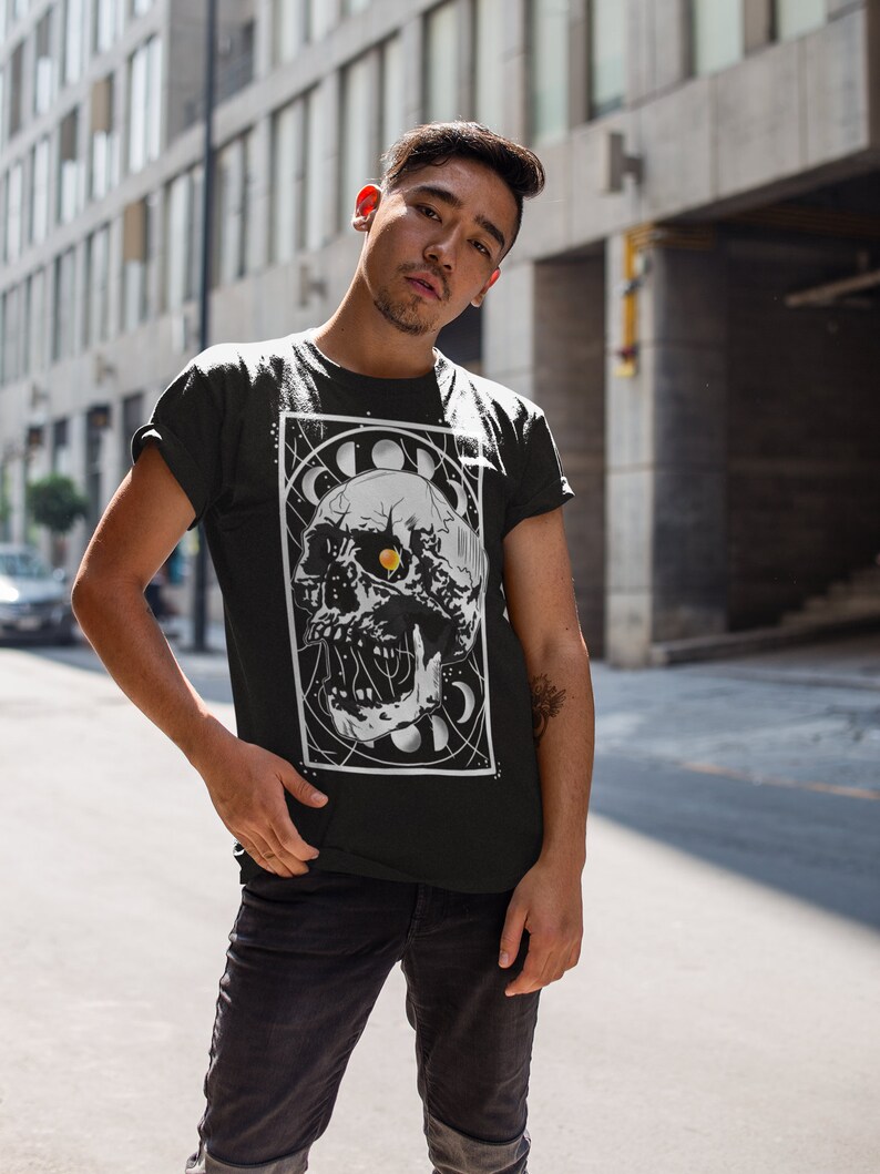 K&ouml;nnte beinhalten: Ein schwarzes T-Shirt mit einem wei&szlig;en Grafikdruck eines Sch&auml;dels mit einem Auge in der Mitte. Der Sch&auml;del ist von einem Kreis aus Monden und Sternen umgeben. Der Text "Cosmic" befindet sich &uuml;ber dem Sch&auml;del.