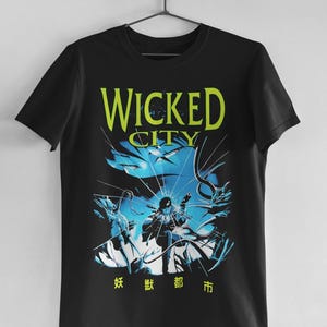 Pode incluir: Camiseta preta com um design gráfico com as palavras "WICKED CITY" em amarelo e uma ilustração azul e branca. O design inclui caracteres japoneses e uma cena dinâmica orientada para a ação.