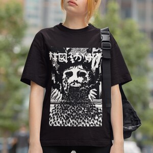 Puede incluir: Una camiseta negra con un estampado gr&aacute;fico blanco de una cara rodeada de un patr&oacute;n de peque&ntilde;as figuras. El gr&aacute;fico incluye texto japon&eacute;s.