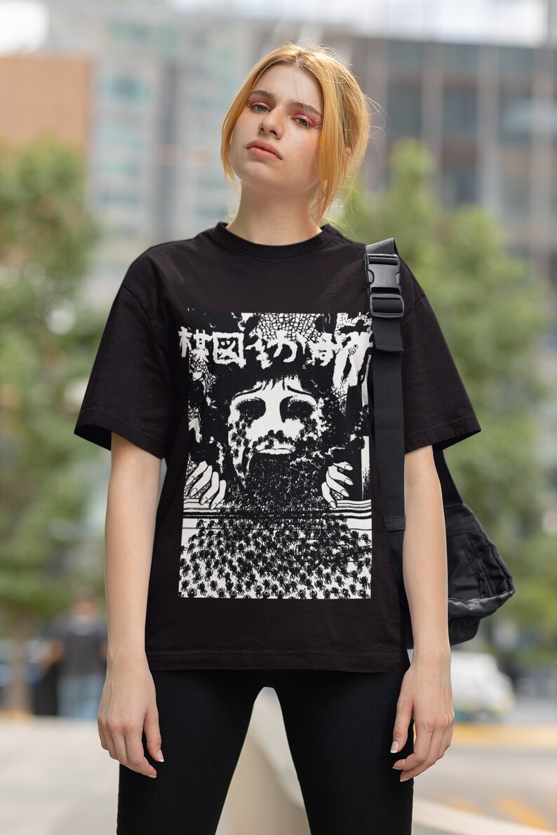 Puede incluir: Una camiseta negra con un estampado gr&aacute;fico blanco de una cara rodeada de un patr&oacute;n de peque&ntilde;as figuras. El gr&aacute;fico incluye texto japon&eacute;s.