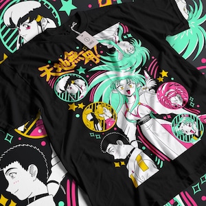 Puede incluir: Camiseta negra con ilustraciones de estilo anime. El diseño presenta personajes en varias poses, texto japonés, estrellas y retratos circulares. La obra de arte utiliza blanco, rosa, amarillo y verde azulado.