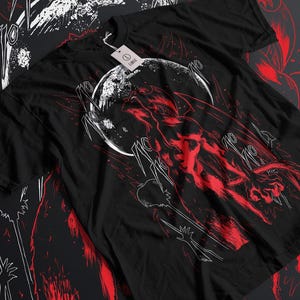 May include: Black t-shirt featuring a red and white graphic design. The design depicts a figure with a moon in the background and Japanese text. The shirt has a tag attached.