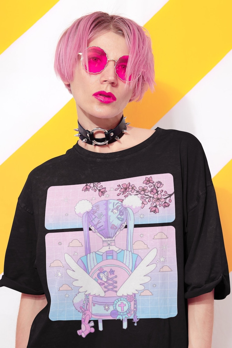 May include: Black t-shirt with a pastel anime-style graphic featuring a character with wings and a backpack. The model is wearing a black studded choker and pink-tinted sunglasses. The background is yellow and white.