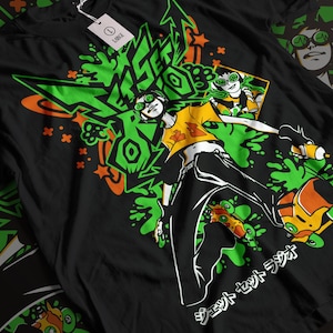 Op de afbeelding: Zwart t-shirt met een opvallend grafisch ontwerp. Het ontwerp toont een figuur met groene bril, een gele top en een zwarte broek, tegen een achtergrond van groene en oranje graffiti-elementen. De tekst "JET SET RADIO" is ook zichtbaar.