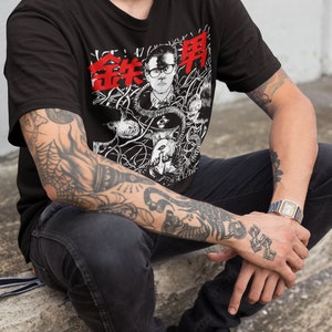 Pode incluir: Uma camiseta preta com uma estampa gr&aacute;fica de um homem usando &oacute;culos e uma m&aacute;scara de g&aacute;s. O gr&aacute;fico &eacute; cercado por um design em preto e branco de fios e outros objetos. O texto "金井申" &eacute; impresso em vermelho na camiseta.