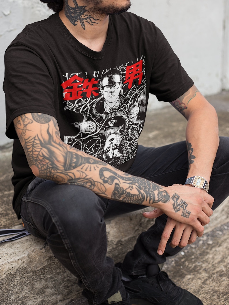 Pode incluir: Uma camiseta preta com uma estampa gr&aacute;fica de um homem usando &oacute;culos e uma m&aacute;scara de g&aacute;s. O gr&aacute;fico &eacute; cercado por um design em preto e branco de fios e outros objetos. O texto "金井申" &eacute; impresso em vermelho na camiseta.