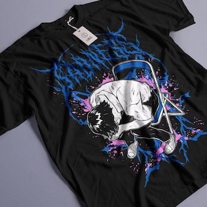 May include: Black t-shirt with a graphic design featuring a person slumped over a blue chair. The design includes blue and pink accents and the word "SADNESS" in blue. A white tag with the word "LARGE" is attached.
