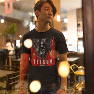 Puede incluir: Una persona lleva una camiseta negra con un estampado gr&aacute;fico de un robot con texto japon&eacute;s que dice "鉄男" (Tetsuo) y "The Iron Man".