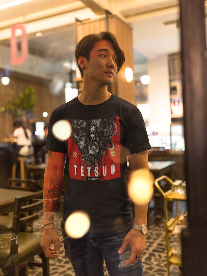 Puede incluir: Una persona lleva una camiseta negra con un estampado gr&aacute;fico de un robot con texto japon&eacute;s que dice "鉄男" (Tetsuo) y "The Iron Man".
