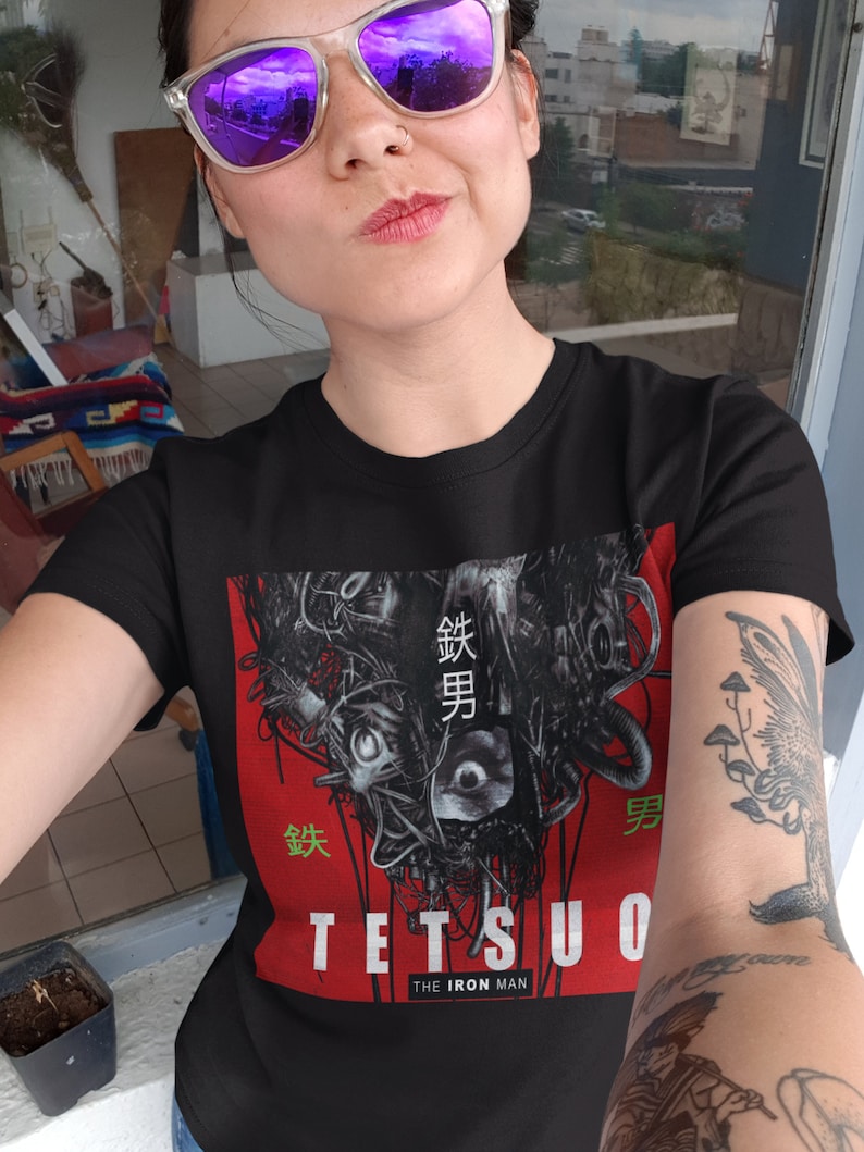 Puede incluir: Una persona lleva una camiseta negra con un estampado gr&aacute;fico de un robot con texto japon&eacute;s que dice "鉄男" (Tetsuo) y "The Iron Man".
