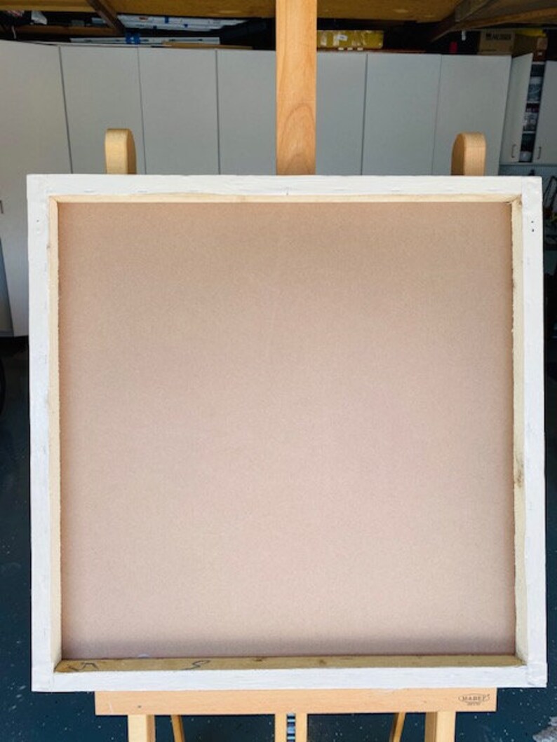 K&ouml;nnte beinhalten: Eine quadratische, hellbraune Leinwand mit wei&szlig;em Holzrahmen, montiert auf einer Holzstaffelei. Die Staffelei hat eine nat&uuml;rliche Holzoberfl&auml;che. Die Leinwand ist leer, bereit zum Malen oder Zeichnen.