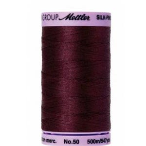 May include: A spool of maroon colored thread labeled "Mettler Silk-Fine No. 50 500m/547yds"