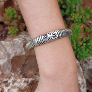 Op de afbeelding: Een zilveren armband met een decoratief ontwerp. De armband is gemaakt van metaal en heeft een gladde, gepolijste afwerking.