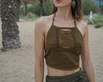 May include: A woman wearing a brown halter top with gold embroidery and a green wrap skirt. She is standing in front of a palm tree and looking off to the side.