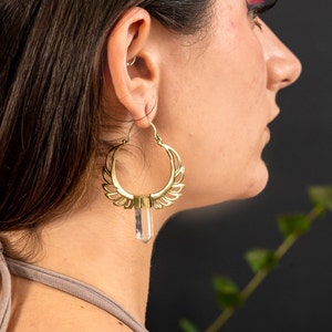 May include: Gold hoop earrings with a clear crystal pendant. The earrings have a delicate, intricate design.
