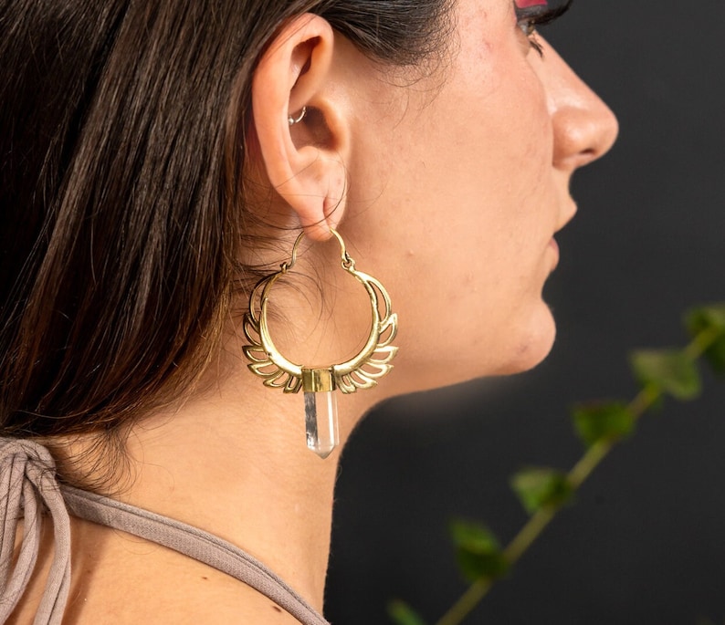 May include: Gold hoop earrings with a clear crystal pendant. The earrings have a delicate, intricate design.