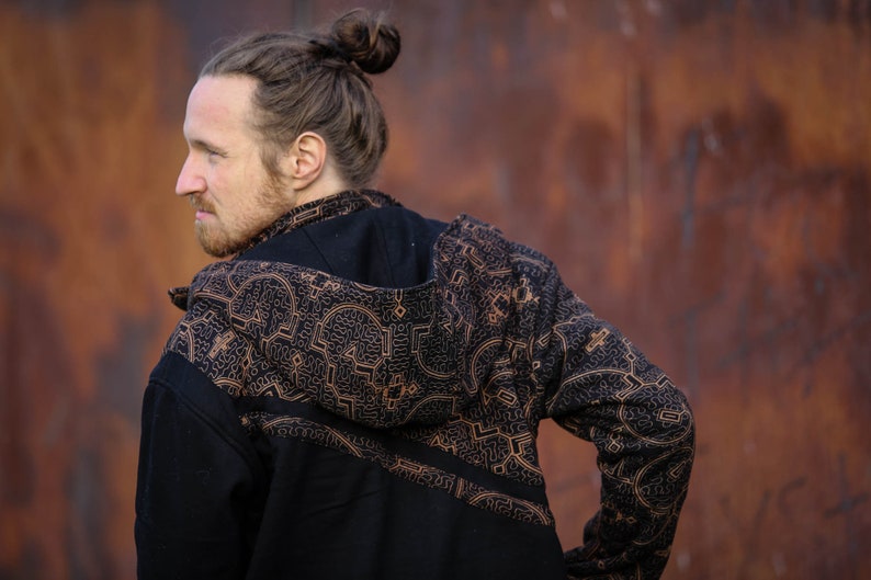 May include: A black hooded jacket with a brown geometric pattern. The jacket has a zipper closure and long sleeves.