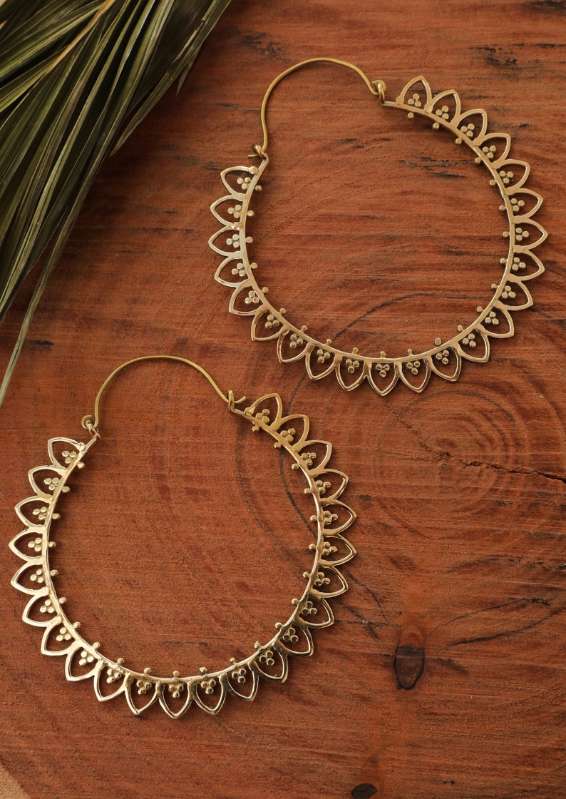 May include: A pair of gold hoop earrings with a delicate, intricate design. The earrings are made of metal and have a circular shape. They are perfect for adding a touch of elegance to any outfit.