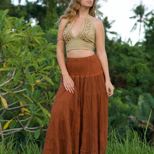 May include: A woman's outfit featuring a halter top and a long skirt. The halter top is a light olive green color with a detailed design around the neckline. The skirt is a tiered, flowing style in a warm, earthy brown. The outfit is suitable for casual wear.