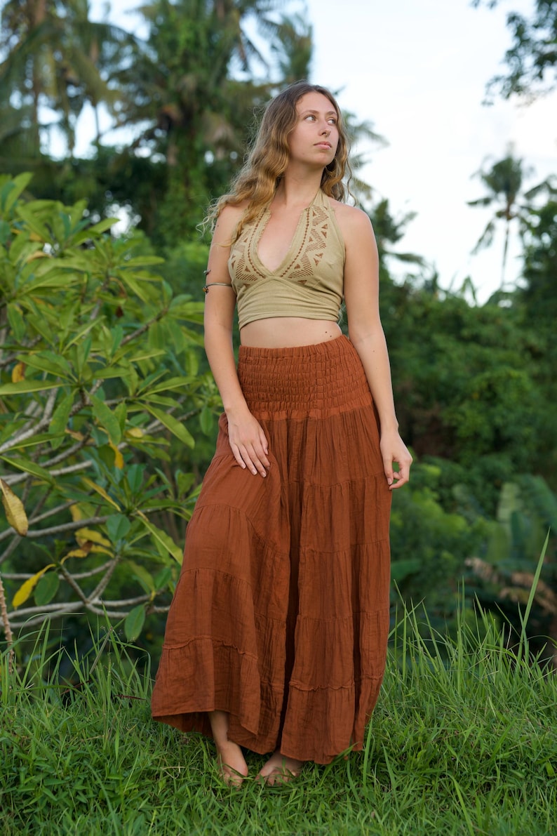 May include: A woman's outfit featuring a halter top and a long skirt. The halter top is a light olive green color with a detailed design around the neckline. The skirt is a tiered, flowing style in a warm, earthy brown. The outfit is suitable for casual wear.