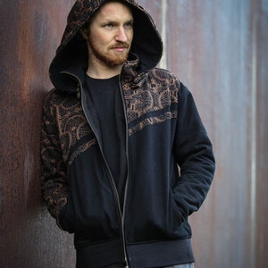 May include: A black zip-up hoodie with a brown patterned design on the front and sleeves. The hoodie has a hood with a drawstring and a zipper closure.