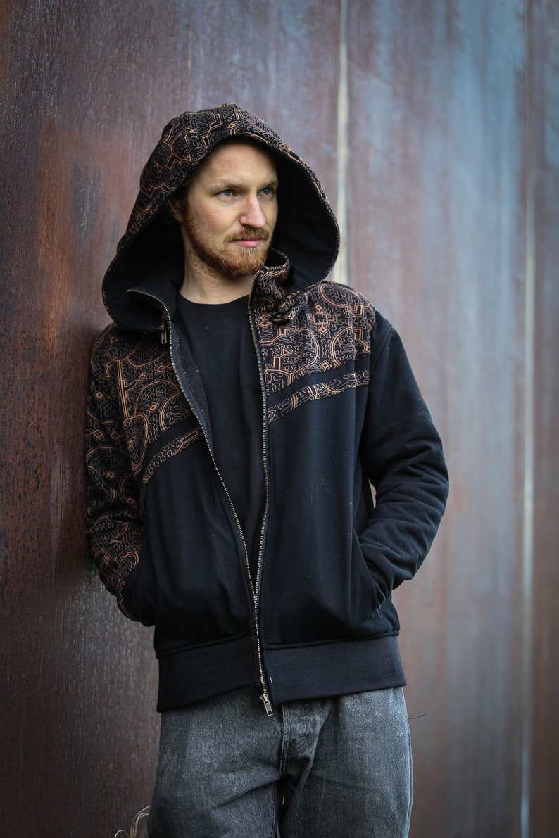May include: A black zip-up hoodie with a brown patterned design on the front and sleeves. The hoodie has a hood with a drawstring and a zipper closure.