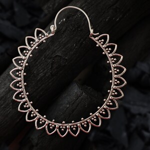 May include: Silver hoop earrings with a delicate floral design. The earrings are circular and have a detailed pattern of small beads and petals.