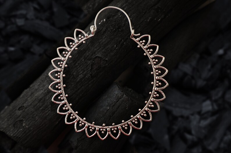 May include: Silver hoop earrings with a delicate floral design. The earrings are circular and have a detailed pattern of small beads and petals.