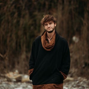 Puede incluir: Una camisa negra de manga larga con ribetes marrones y una bufanda a juego. La camisa tiene un corte holgado y est&aacute; hecha de un material suave. El modelo lleva pantalones negros.