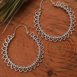 May include: A pair of silver hoop earrings with a delicate floral design. The earrings are large and have a circular shape.