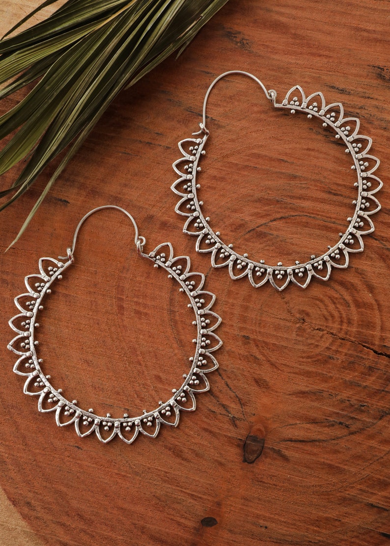 May include: A pair of silver hoop earrings with a delicate floral design. The earrings are large and have a circular shape.