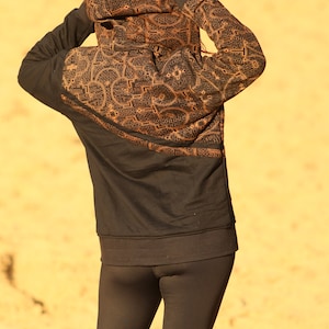 May include: A black hoodie with a geometric pattern in orange. The hoodie is worn by a person with black leggings.
